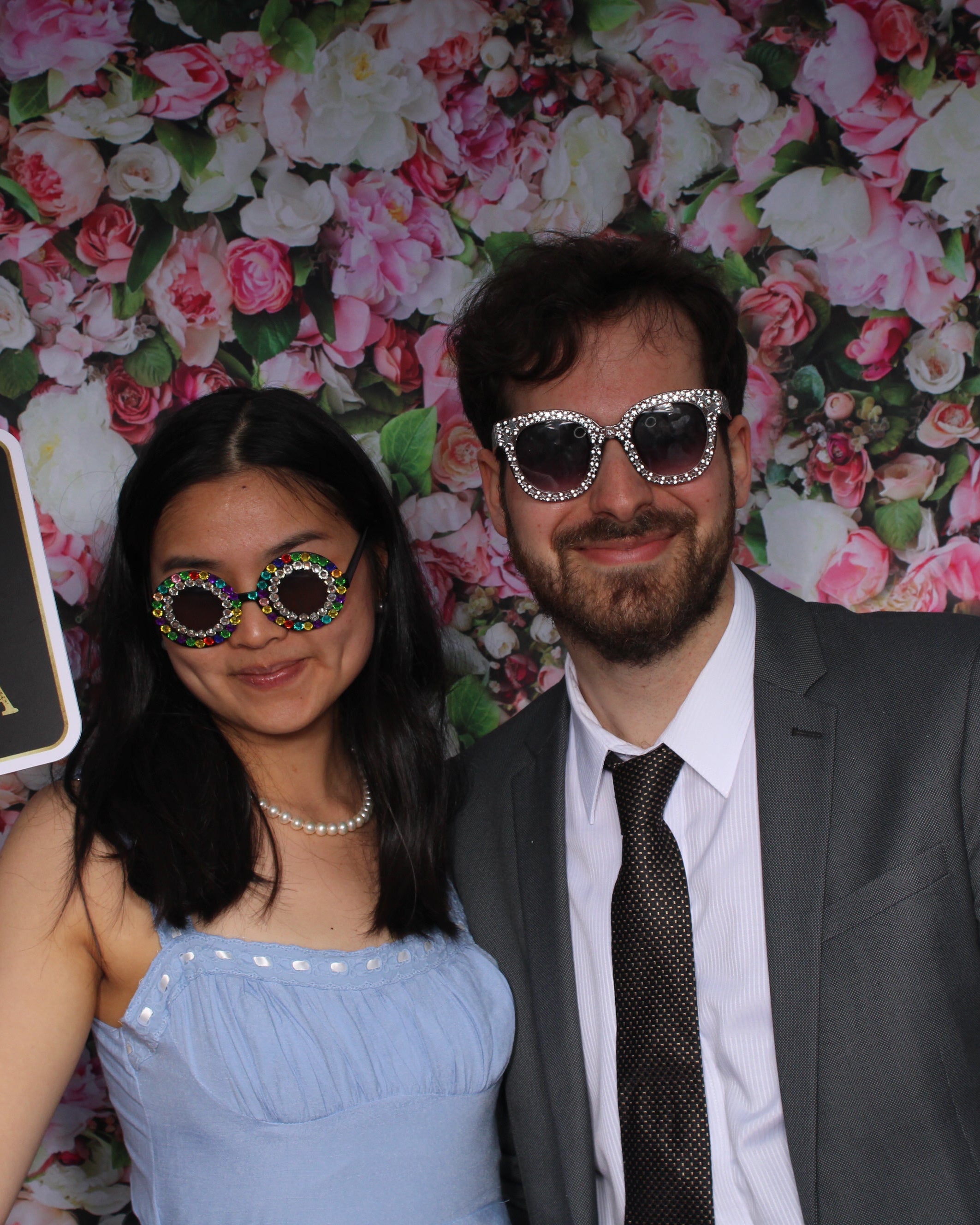 Two people posing with props in front of a floral backdrop