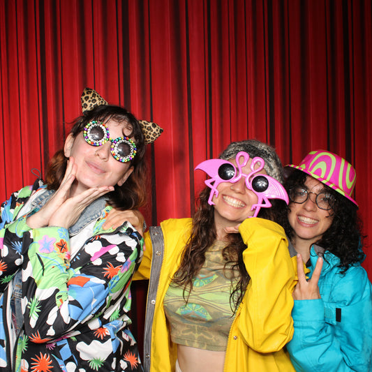 Three people posing with props in front of a red curtain