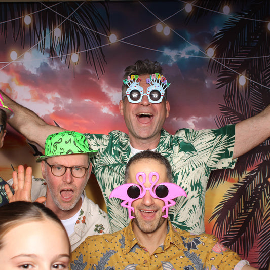 Group of people with colorful props in a photo booth with a tropical background